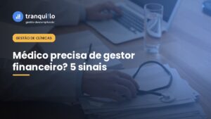 Médico de jaleco entre laptop, papelada e estetoscópio, representando a rotina financeira do consultório